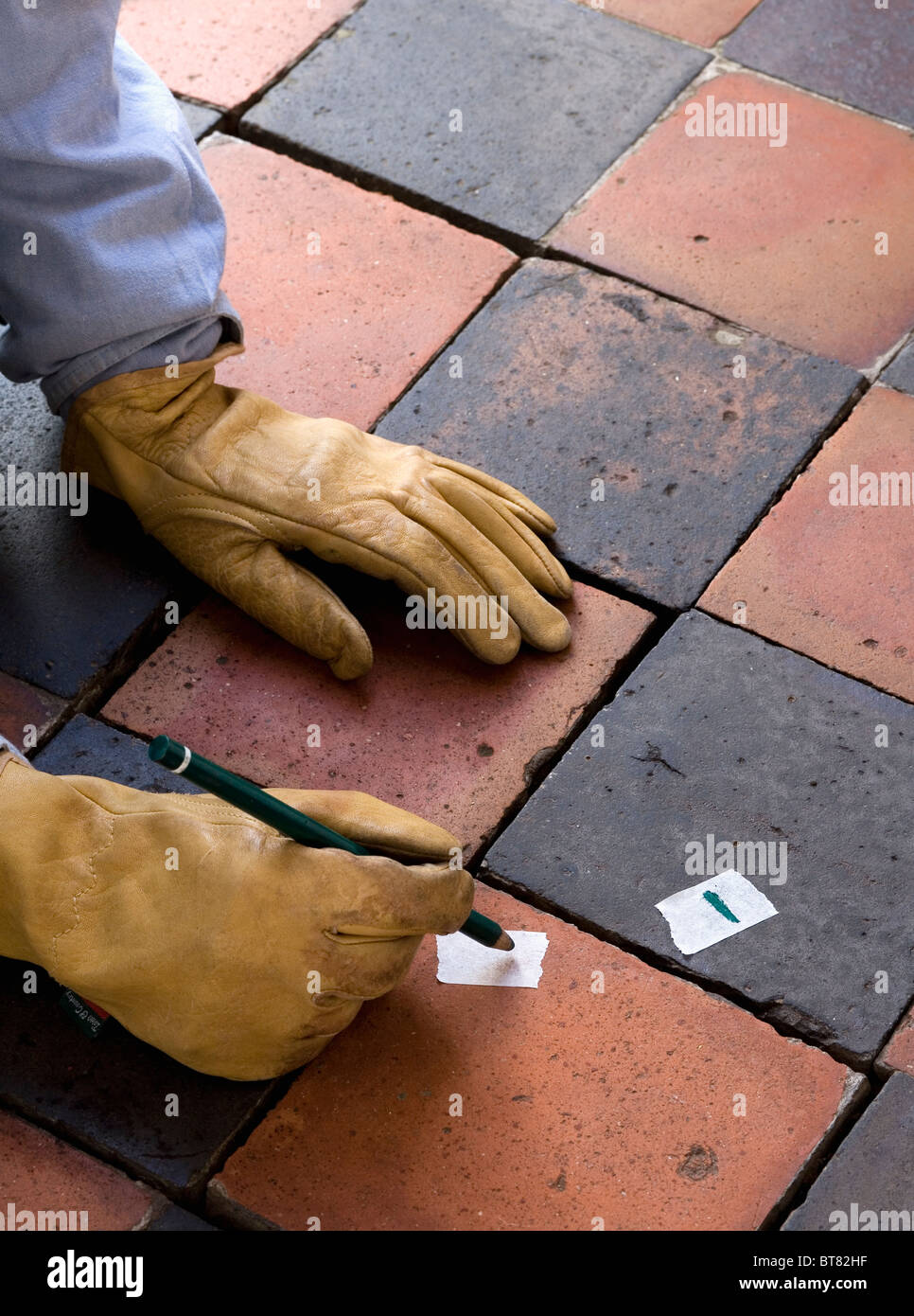 Nahaufnahme der Hände in Schutzhandschuhe auf alten Schwarz + Terrakotta Steinbruch gefliesten Boden Stockfoto