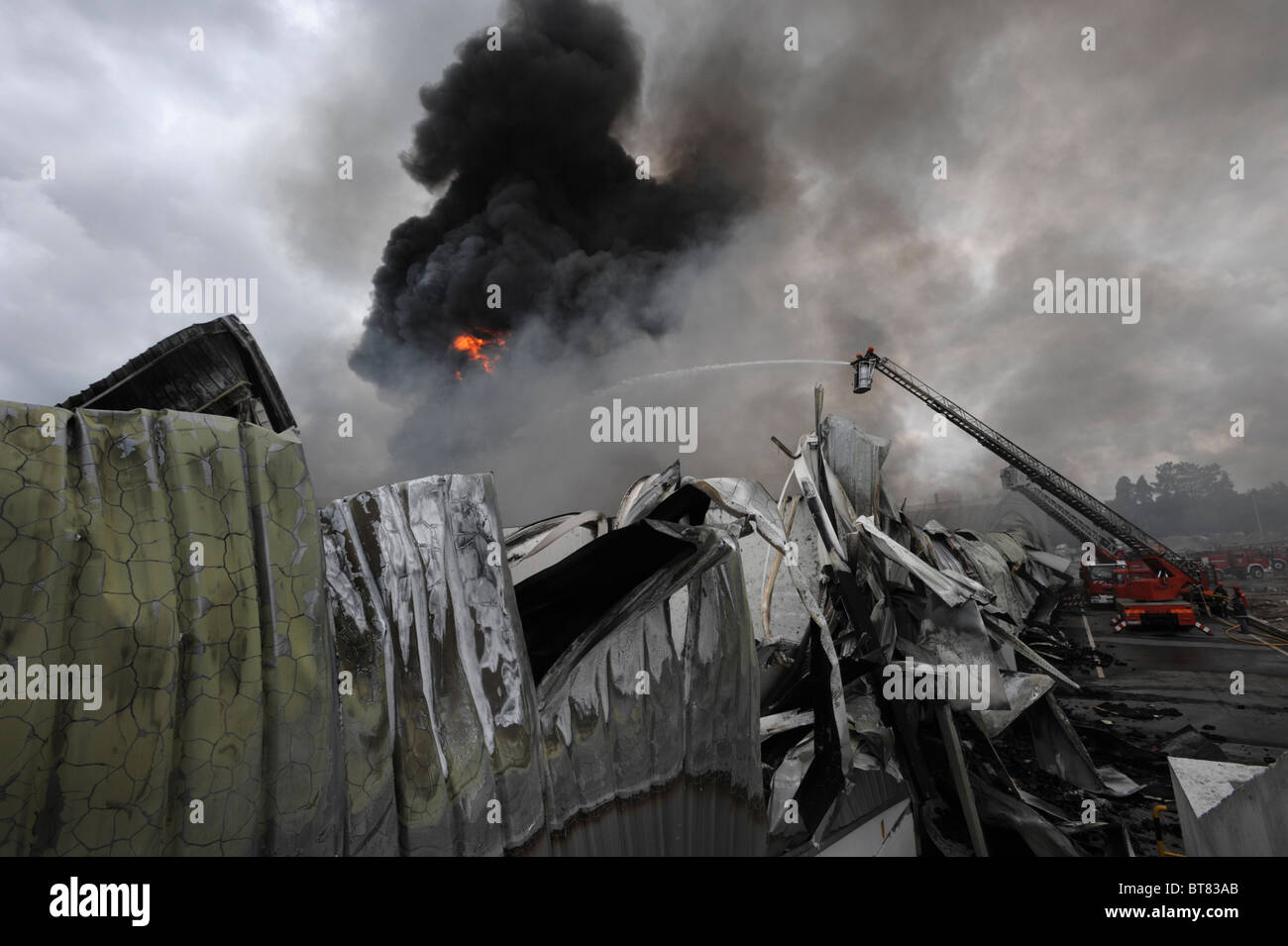 Feuerwehr auf eine Ausziehleiter Löschangriff eine massive Fabrik inmitten dichten Rauch Stockfoto