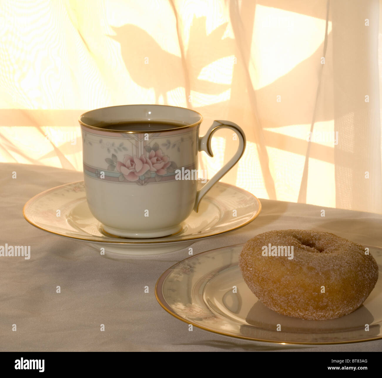 Ein sonniger Morgen mit Kaffee und Krapfen zum Frühstück, mit einem Vogel auf dem Baum vor dem Fenster. Stockfoto