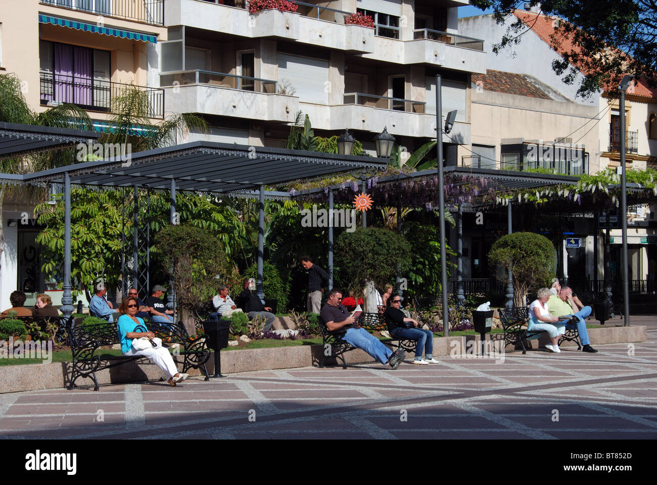 Menschen sitzen auf Bänken in der Plaza De La Constitución, Fuengirola, Costa del Sol, Provinz Malaga, Andalusien, Spanien. Stockfoto