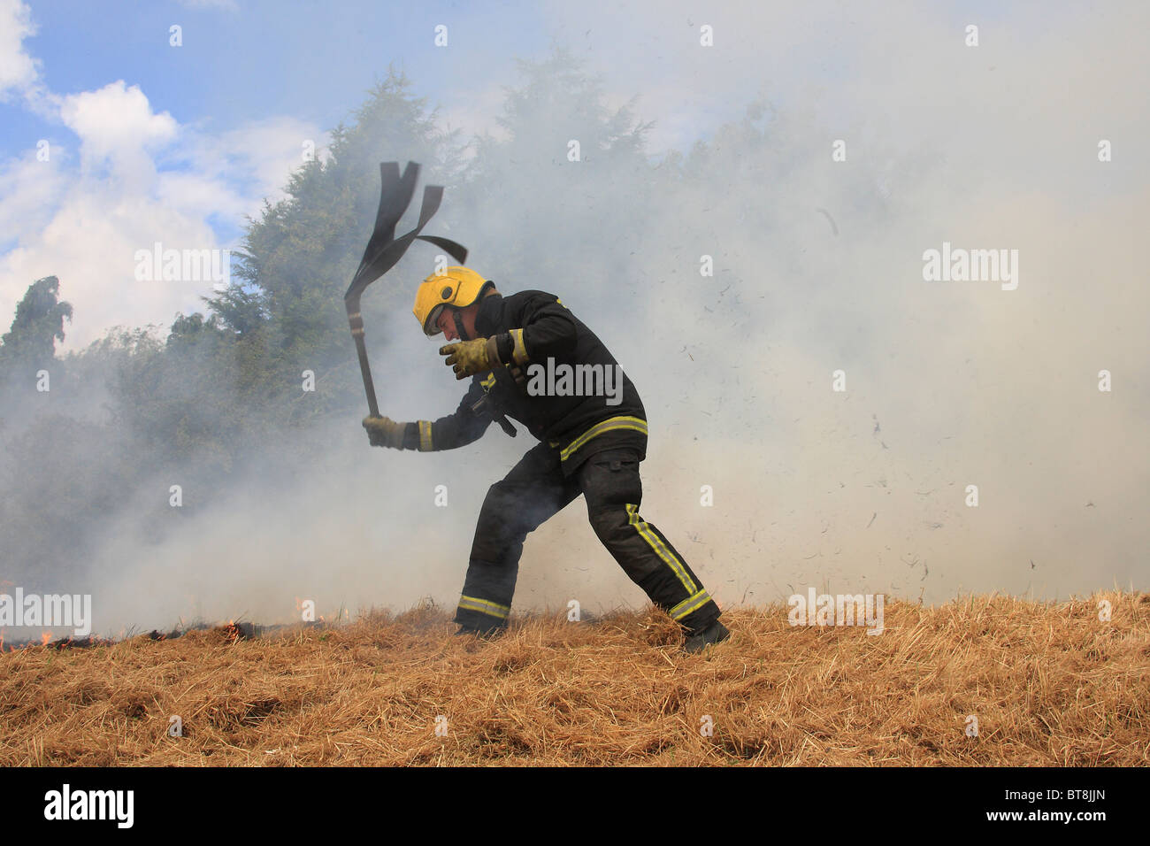 Feuerwehrmann mit einem Schneebesen zu einem Feld Feuer zu bekämpfen Stockfoto