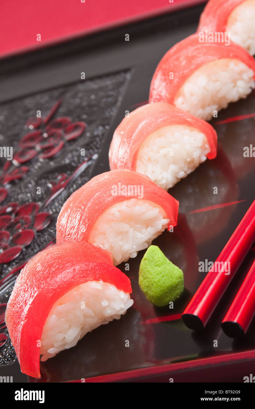 Frischen roten Thunfisch Nigiri Sushi mit roten Stäbchen auf einem geschnitzten hölzernen Tablett mit leuchtend grünen wasabi Stockfoto