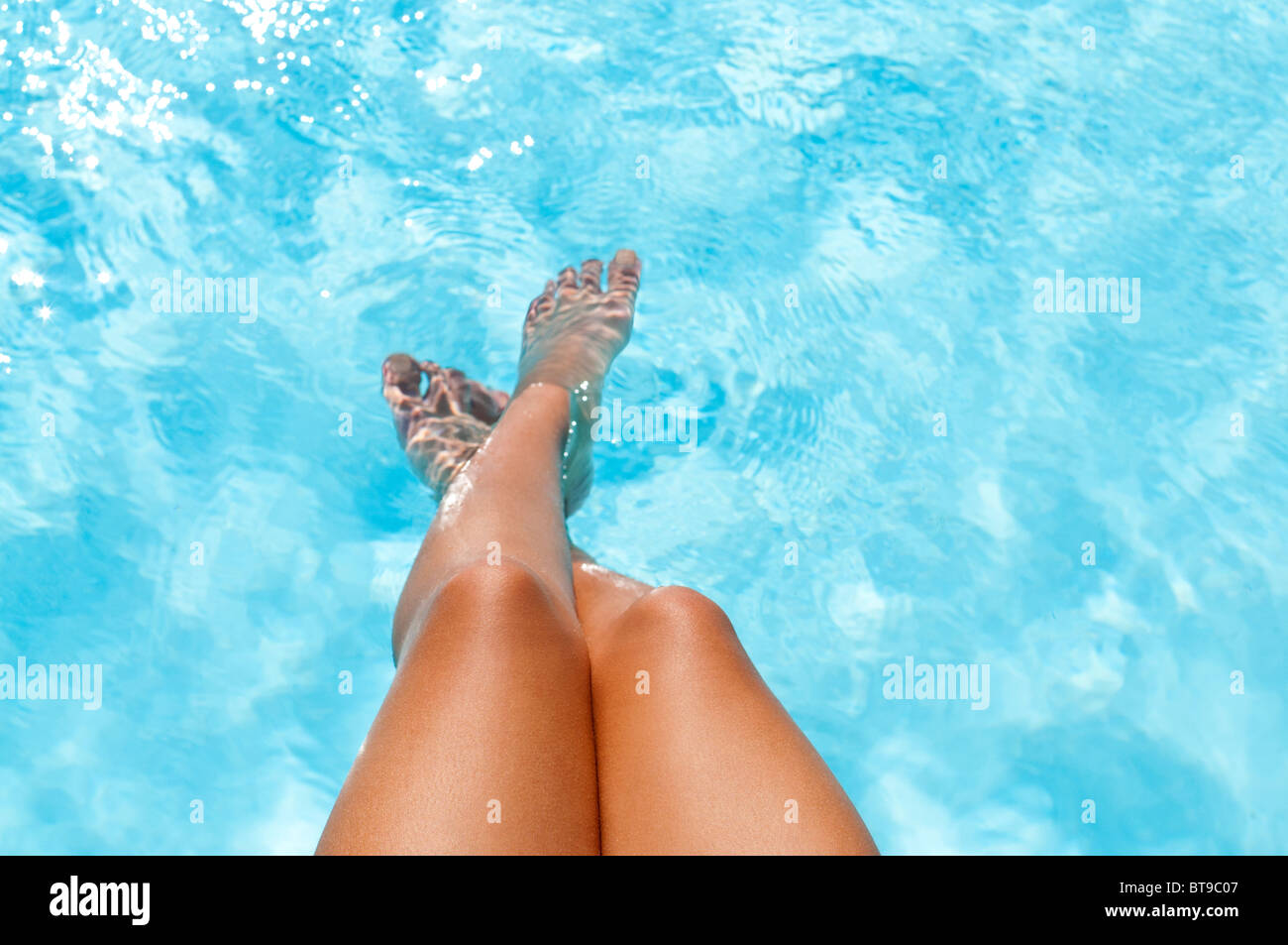 Eine junge Frau, die ihre Füße in ein Schwimmbad tauchen Stockfoto