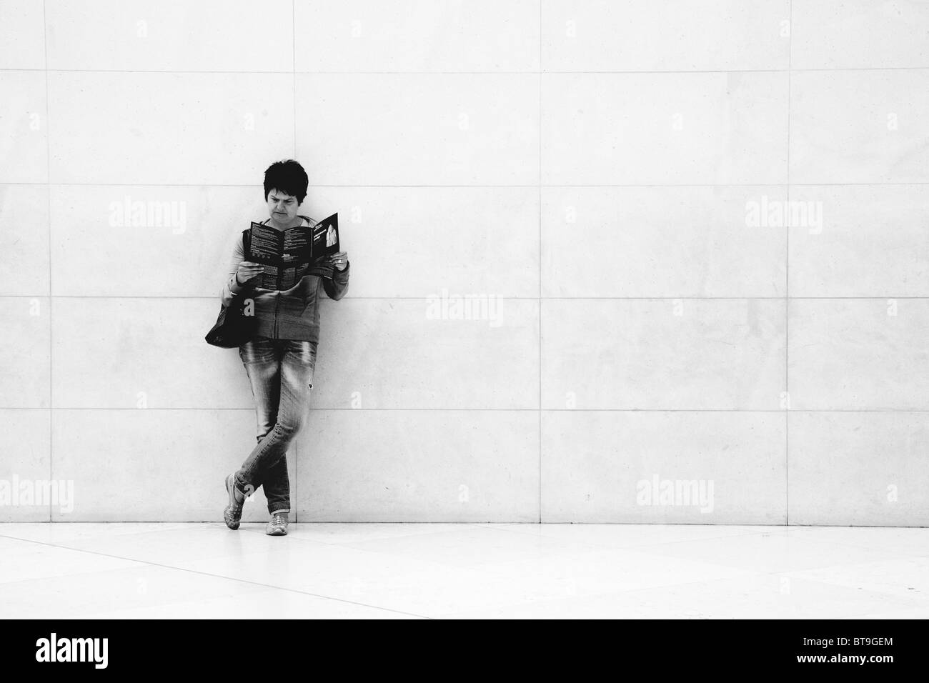 Eine Frau steht allein gegen die Wand beim Lesen einer Zeitschrift im British Museum in London Stockfoto