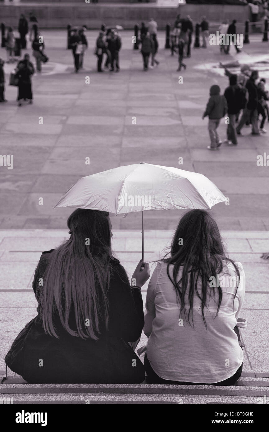 Zwei Mädchen sitzen auf der Treppe am Trafalgar Square im Regen Stockfoto