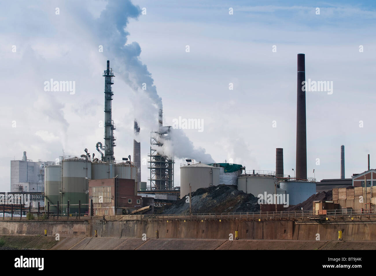 Duisburger Hafen, große Öllagertanks Haufen Kohle und Rauchen Industrieschornsteine im Abendlicht, North Rhine-Westphalia Stockfoto