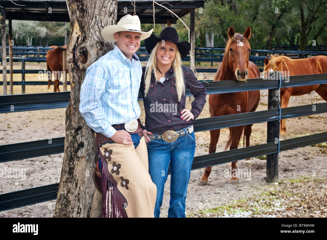 Junge und attraktive Cowboy und Cowgirl talking beim stehen vor einer Koralle Pferd auf einer ranch Stockfoto