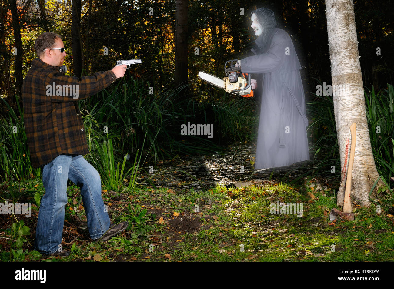 Gespenst der Ghoul mit einer Kettensäge angreifen, ein Mann mit einer Pistole durch einen Teich im Wald bei Halloween Stockfoto