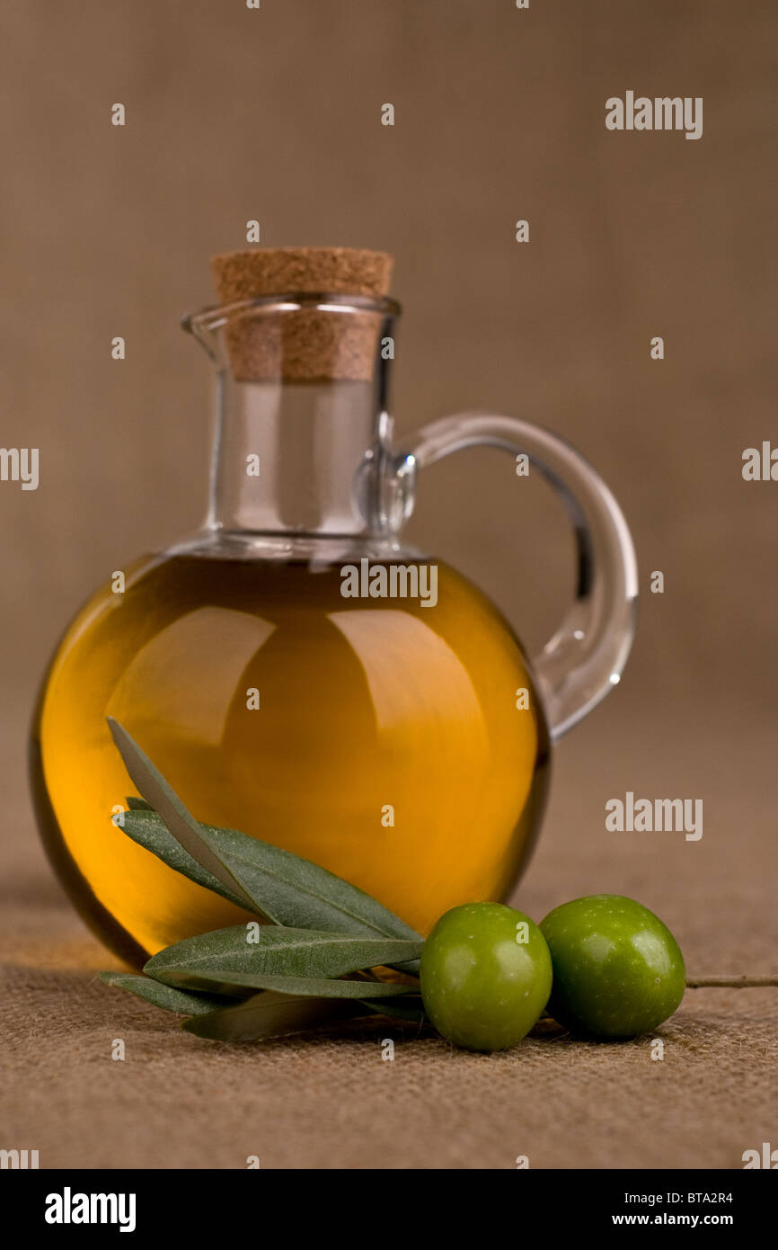 Grüne Oliven auf einem Zweig und einer Flasche Olivenöl, Sackleinen Hintergrund Stockfoto
