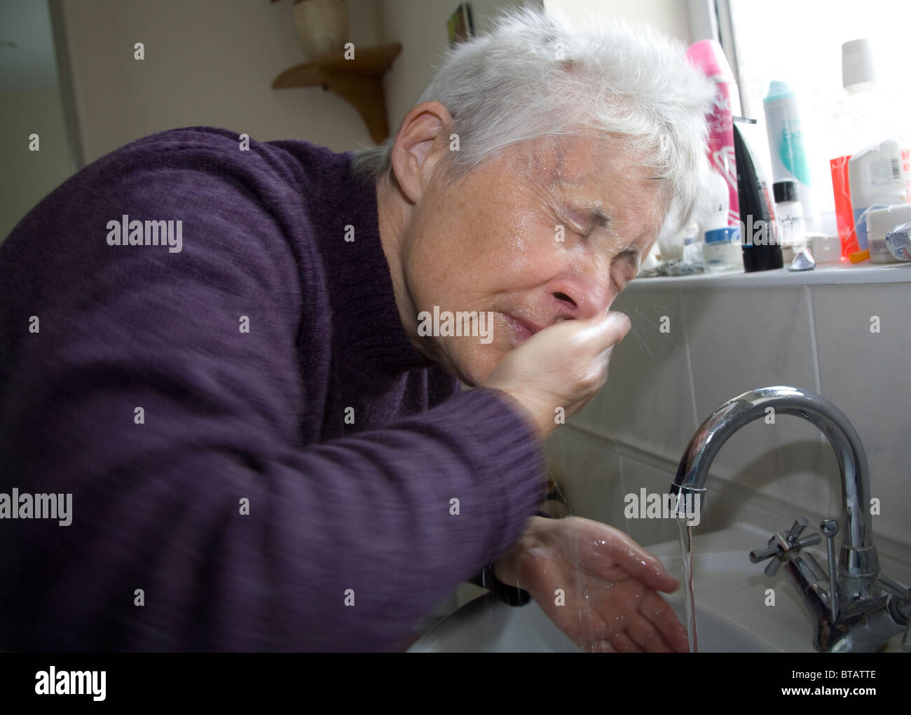 Nahaufnahme von grauen Haaren Seniorin saufen Gesicht abwaschen im Badezimmer Waschbecken Stockfoto