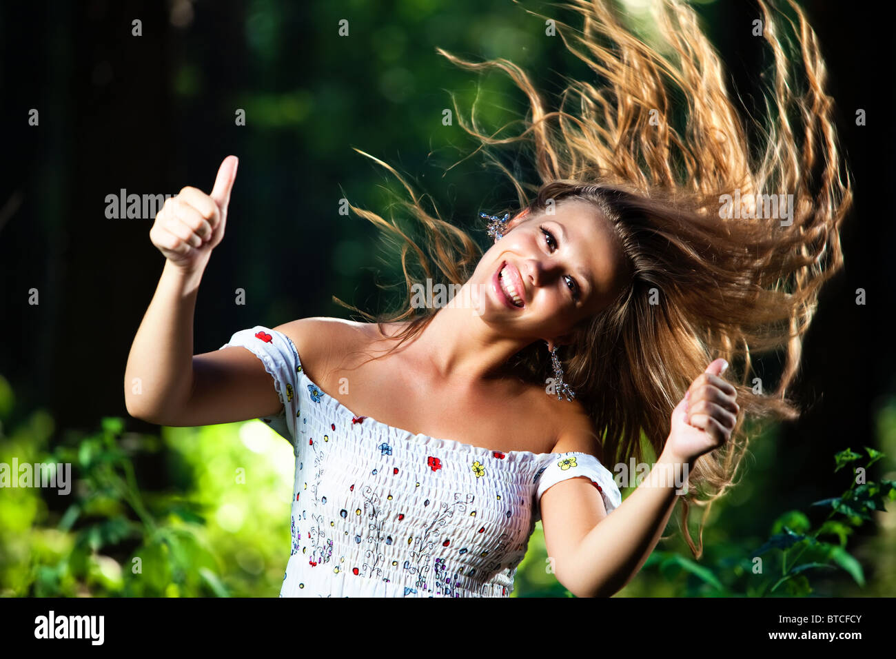 Junge, lächelnde Frau mit wehenden Haaren zeigt Erfolg Handsign. Stockfoto