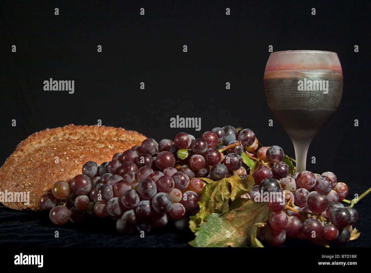 Stillleben mit Brot, rote Weintraube und Glas Rotwein auf schwarzem Hintergrund. Stockfoto
