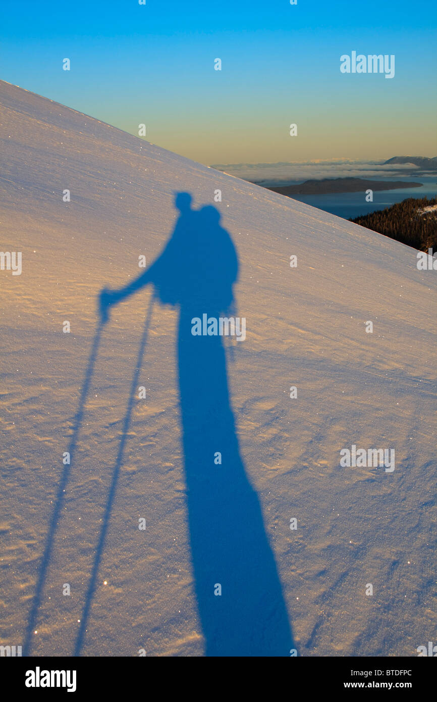 Ein Skifahrer wirft einen langen Schatten über den Schnee in der Morgendämmerung, als er einen Berg auf Wrangell Island, Alaska besteigt Stockfoto