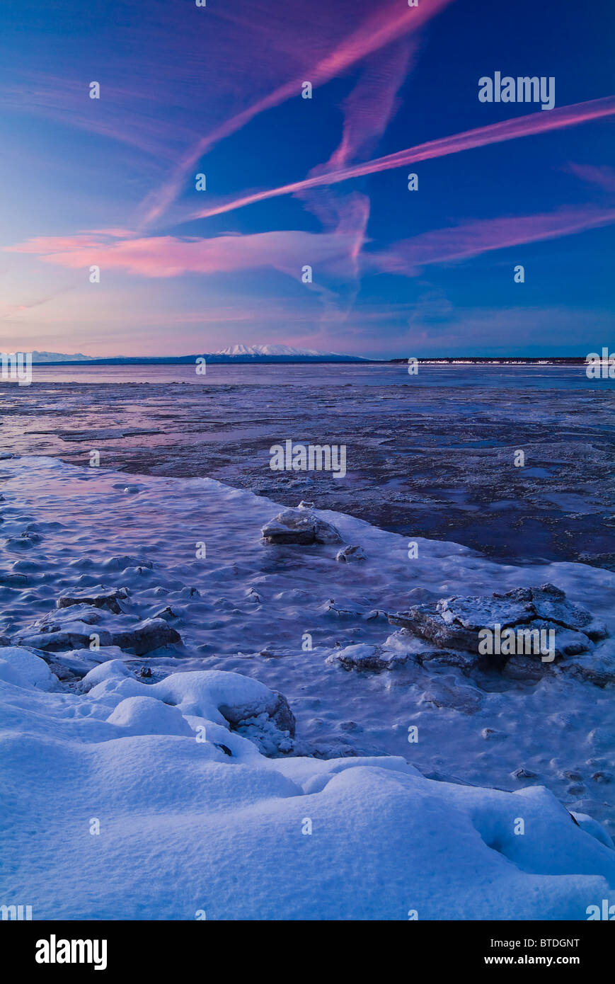 Kondensstreifen des Flugverkehrs säumen den Himmel bei Sonnenuntergang über Cook Inlet mit Mount Susitna im Hintergrund, Alaska Stockfoto