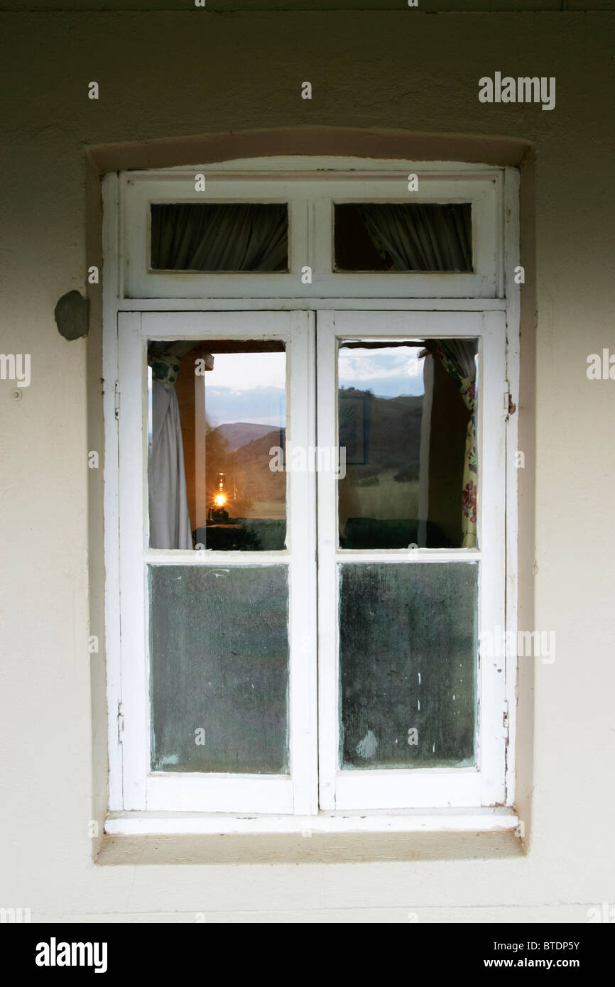 Blick durch eine alte weiße gerahmte Holzfenster und eine beleuchtete Petroleumlampe sichtbar im Inneren Stockfoto