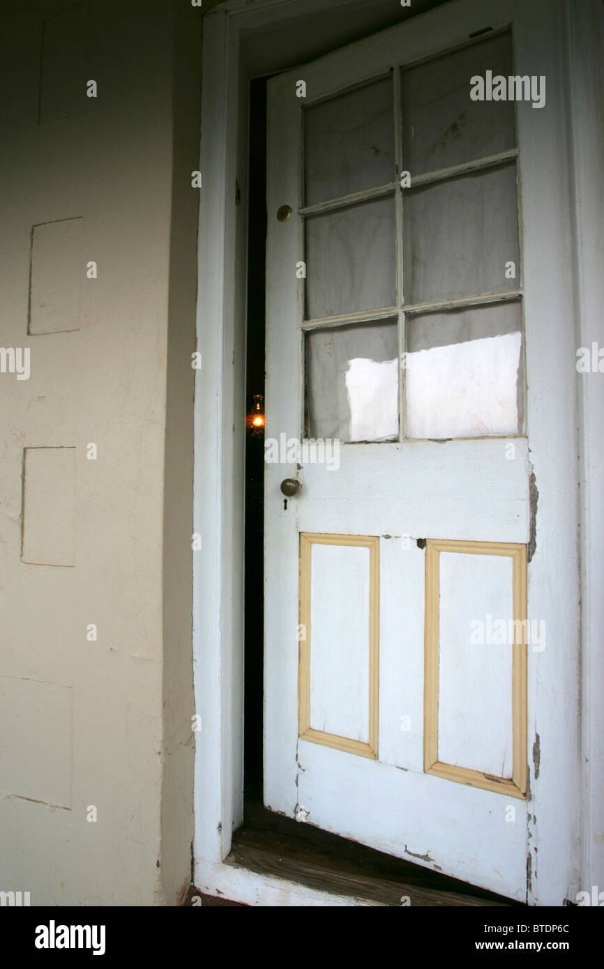 Eine alte weiße Holztür links Spalt mit dem schwachen Licht aus einer Petroleumlampe nur sichtbar Stockfoto