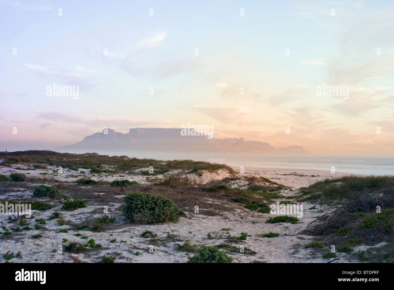Ein Blick über die Dünen an der Küste bei Sonnenuntergang in Richtung Tafelberg in der Ferne Stockfoto