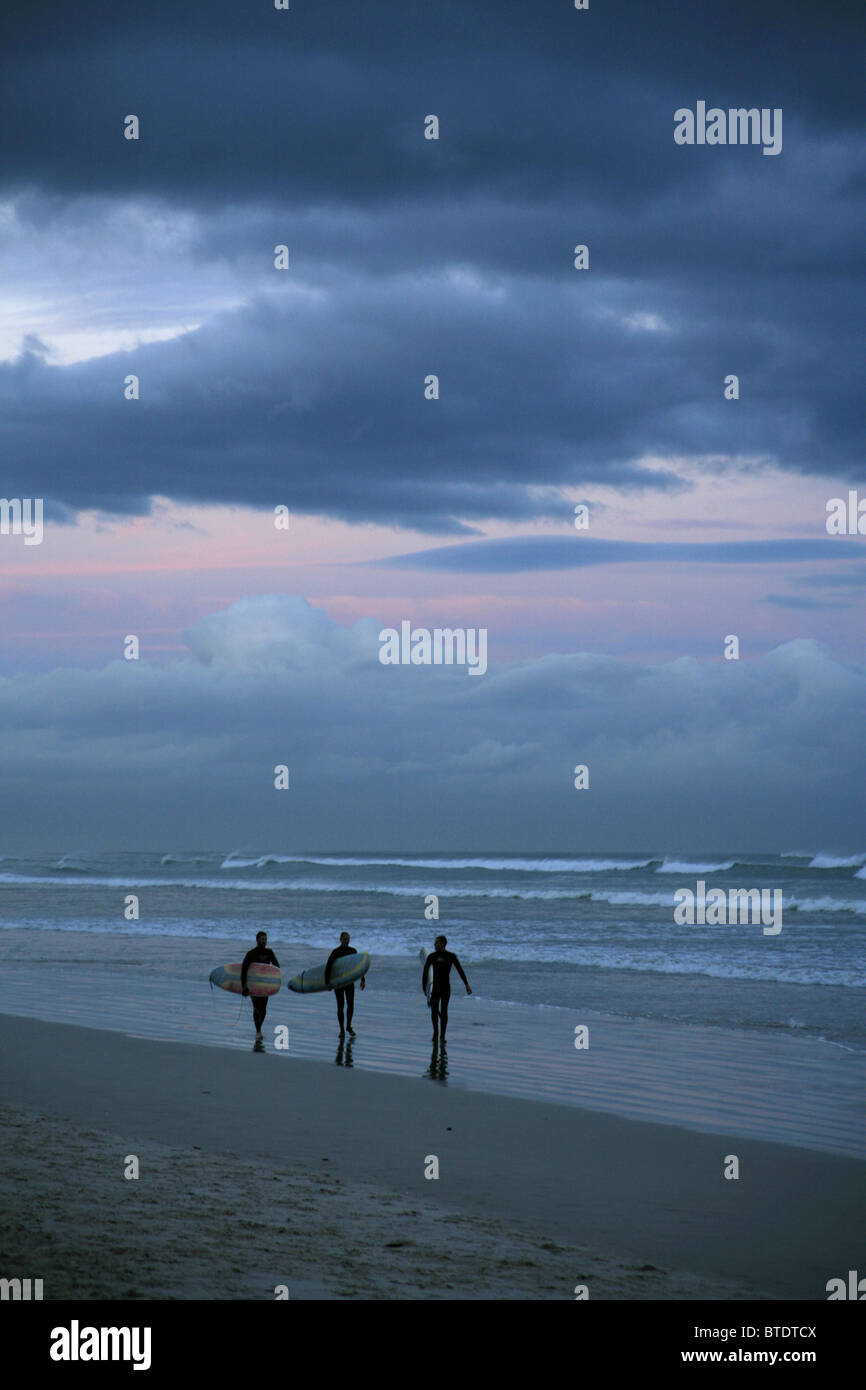 Surfer gehen nebeneinander bei stürmischem Wetter am Muizenberg Strand entlang mit ihren Surfbrettern, versteckt unter dem Arm Stockfoto