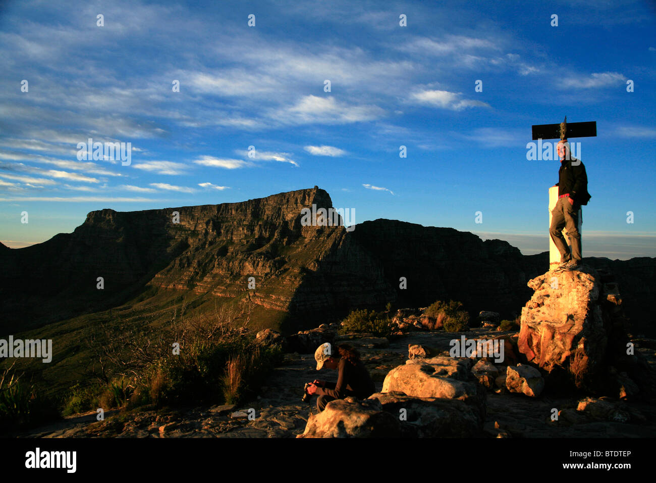 Wanderer auf den Lions Head bei Sonnenaufgang mit dem Tafelberg im Hintergrund Stockfoto