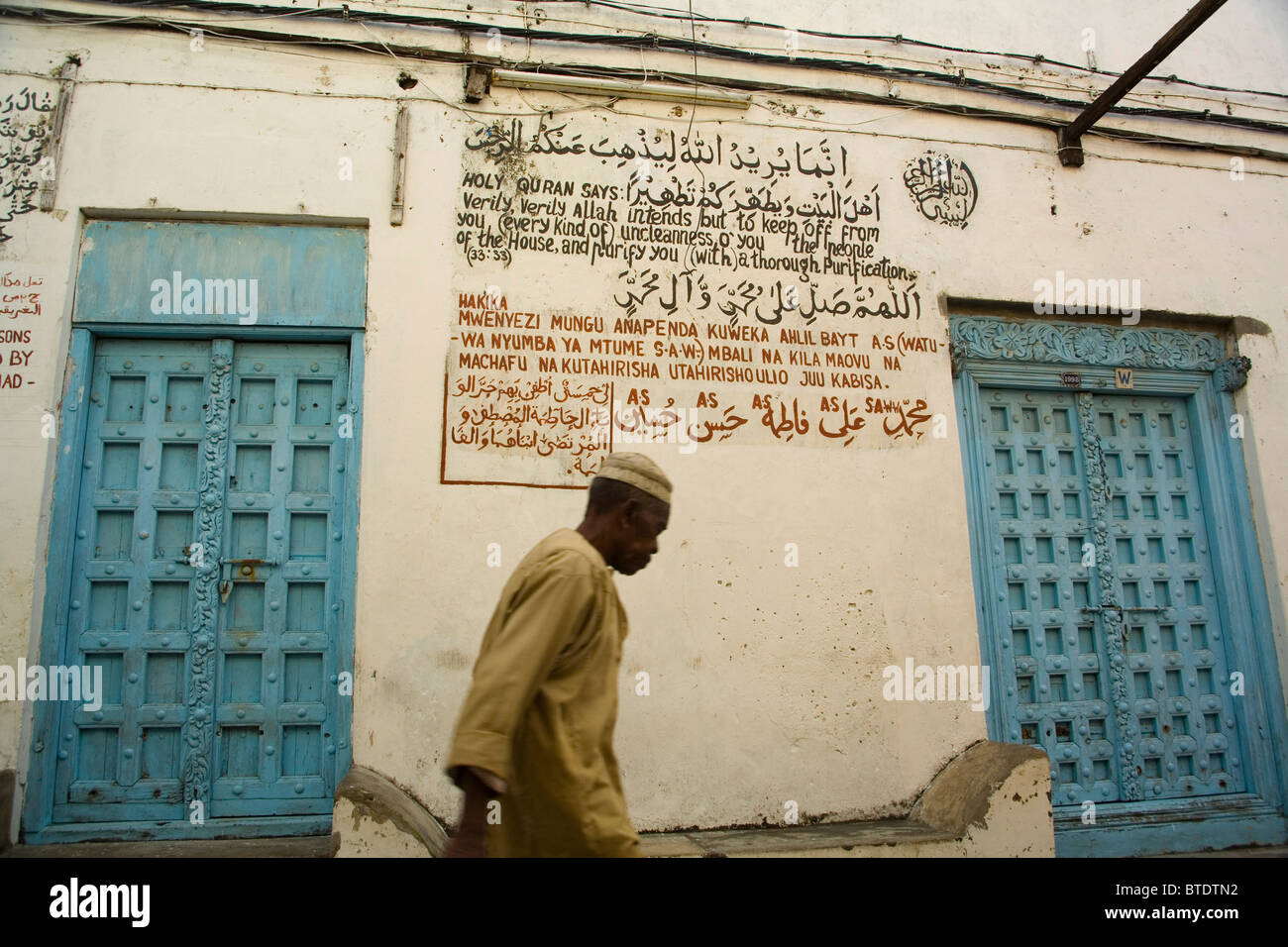 Muslimischen Mann zu Fuß vorbei an einer Moschee mit Koran Zitaten an die Wand geschrieben Stockfoto