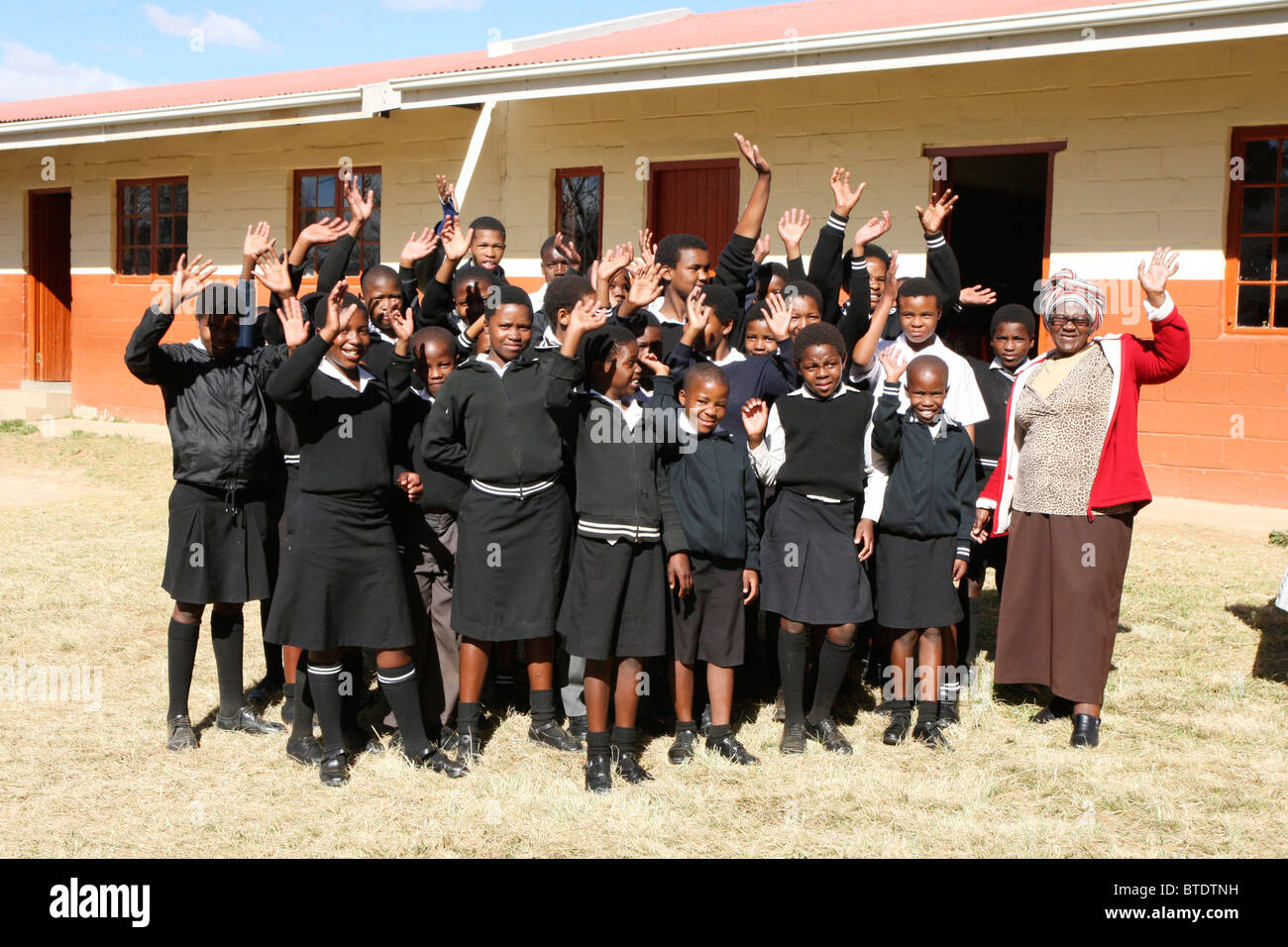 Gruppe von ländlichen Schülerinnen und Schüler und ihre Lehrer winken außerhalb einer Klasse in einer ländlichen Schule in Kwazulu-Natal Stockfoto