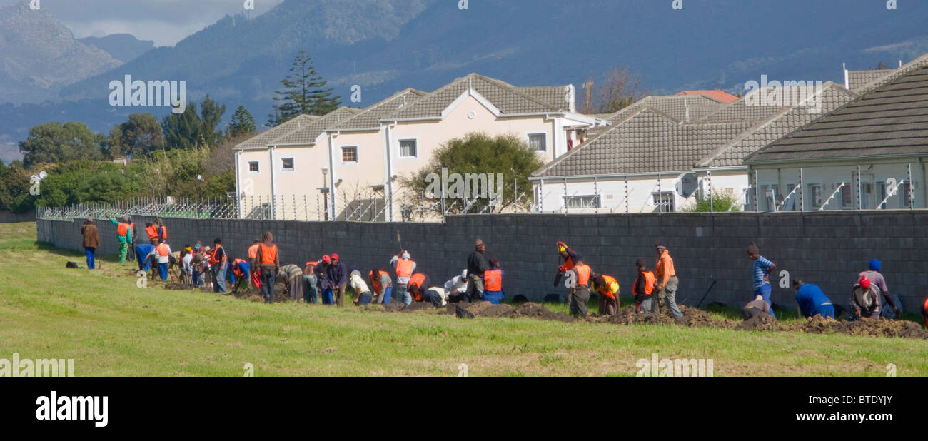 Städtische Arbeiter graben eine Entwässerungsrinne außerhalb einer Sicherheitskomplex Stockfoto