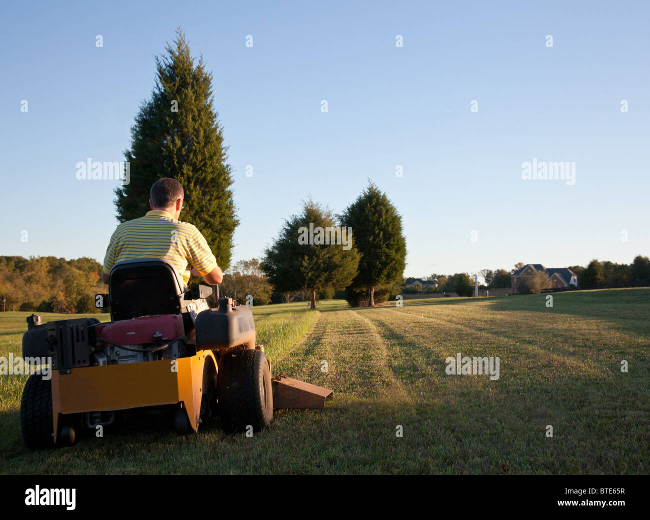 Mann mittleren Alter auf Null drehen Rasenmäher Ausschnittgras an einem sonnigen Tag mit der Sonne niedrig am Himmel Stockfoto