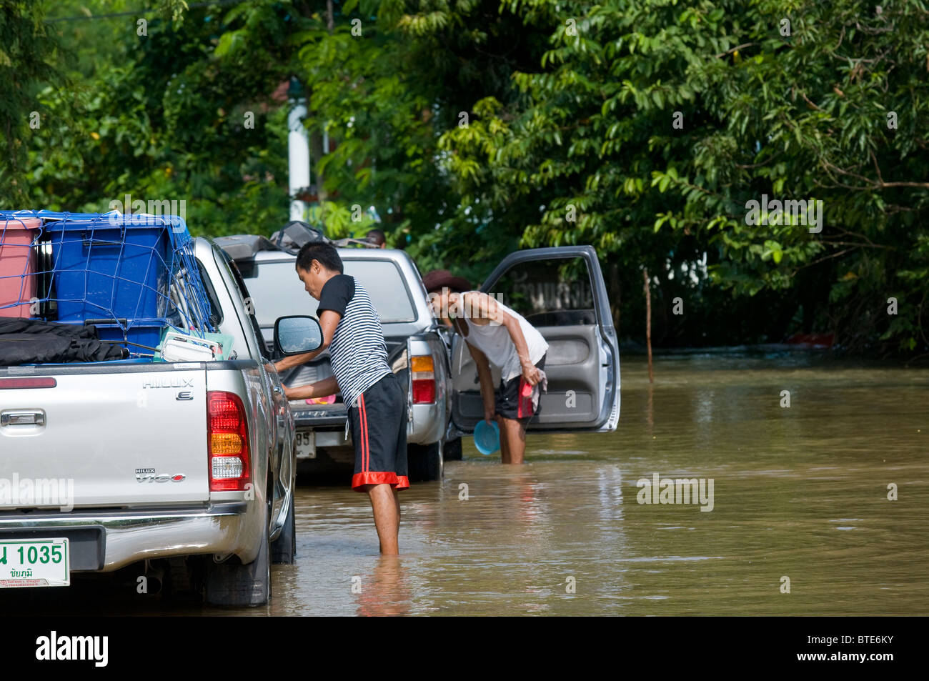 Dorfbewohner, die Reinigung ihrer Pickup-Trucks in das Wasser von einer überfluteten Straße in Thailand Stockfoto