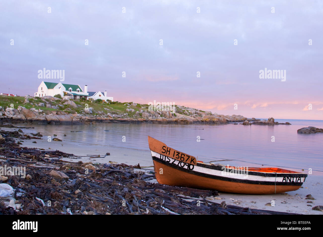 Angelboot/Fischerboot vor Anker an einem Strand mit einem großen Cape Dutch Haus im Hintergrund Stockfoto