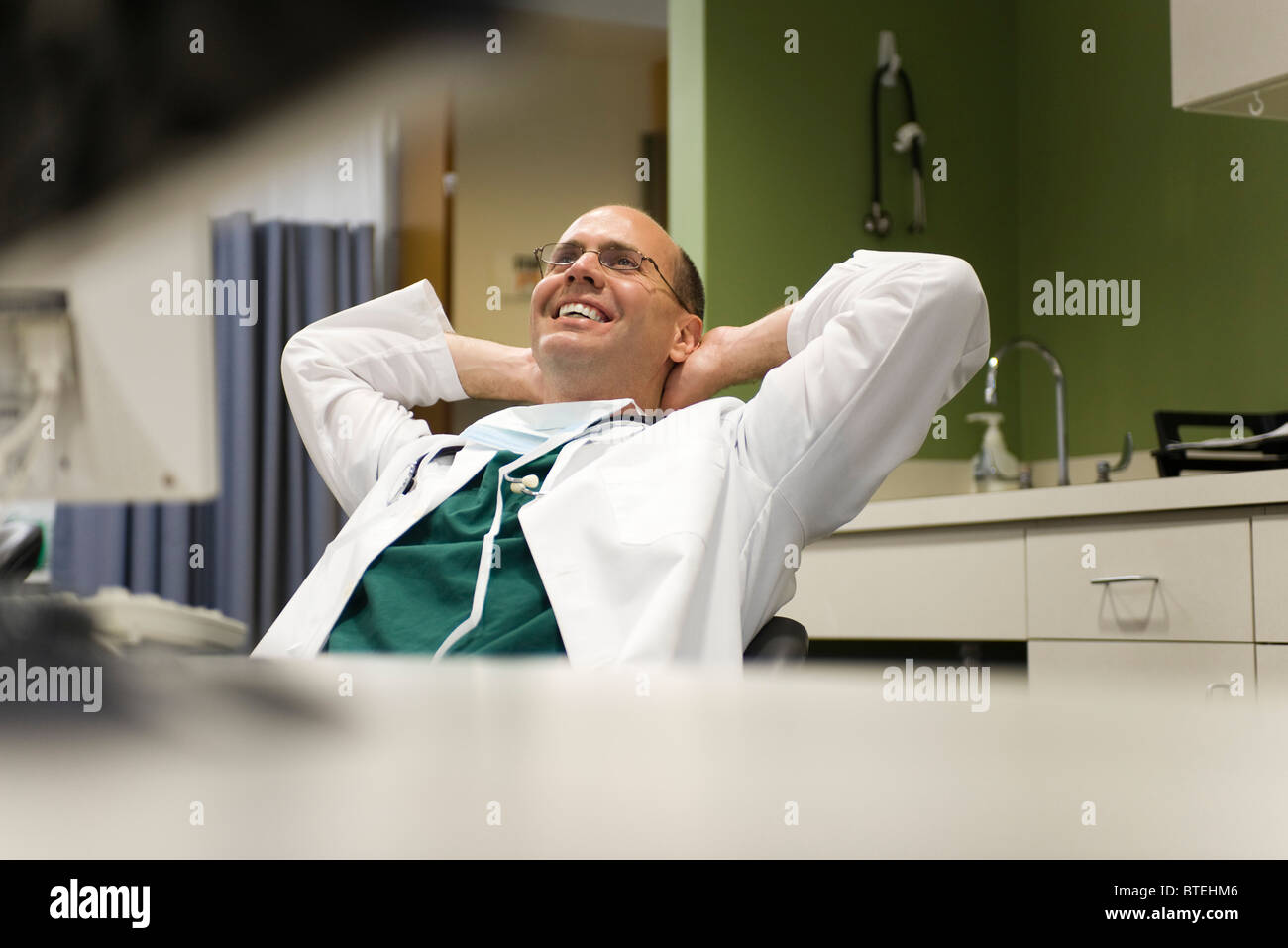 Arzt lehnt sich zurück in den Stuhl mit Händen hinter dem Kopf, lächelt Stockfoto