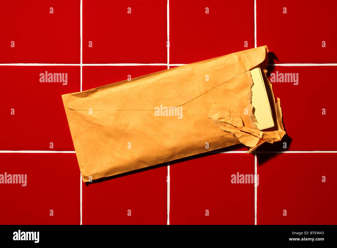 Eine gebrauchte mailing Postumschlag aufgerissen. Rot gekachelter Hintergrund Stockfoto