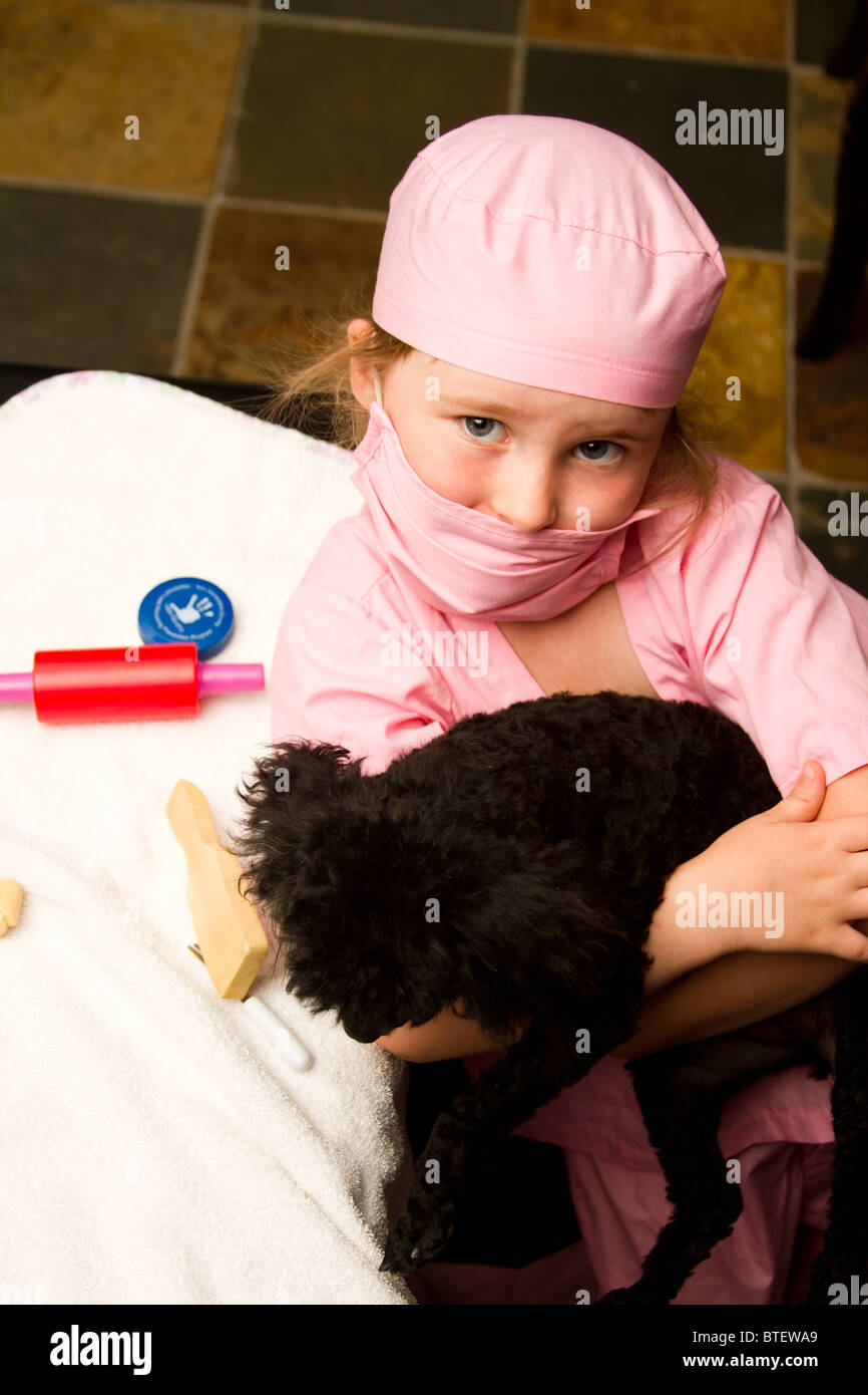 Junges Mädchen verkleidet, wie ein Arzt oder Tierarzt in rosa hilft kleinen Pudelhund Stockfoto