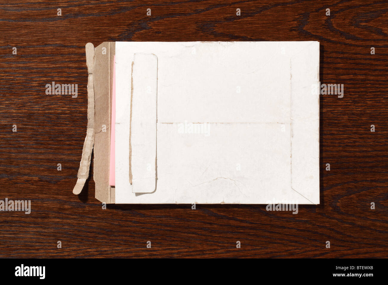 Eine gebrauchte mailing Postumschlag aufgerissen. Eine dunkle braune Holz Schreibtisch-Hintergrund Stockfoto