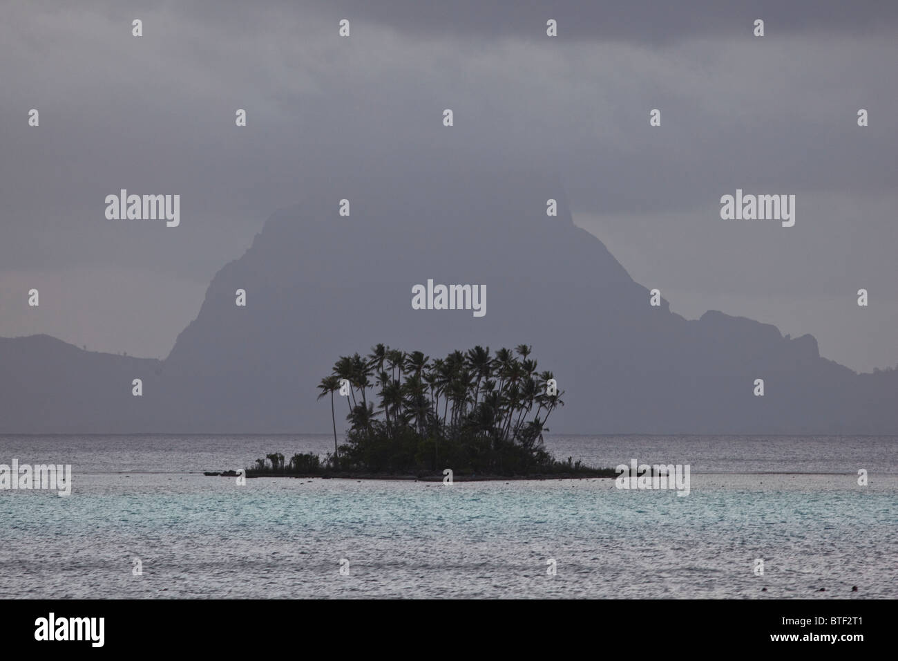 Wolken über der vulkanischen Insel Bora Bora und eine kleine, sandige Inselchen von Kokospalmen, Cocos Nucifera abgedeckt. Stockfoto