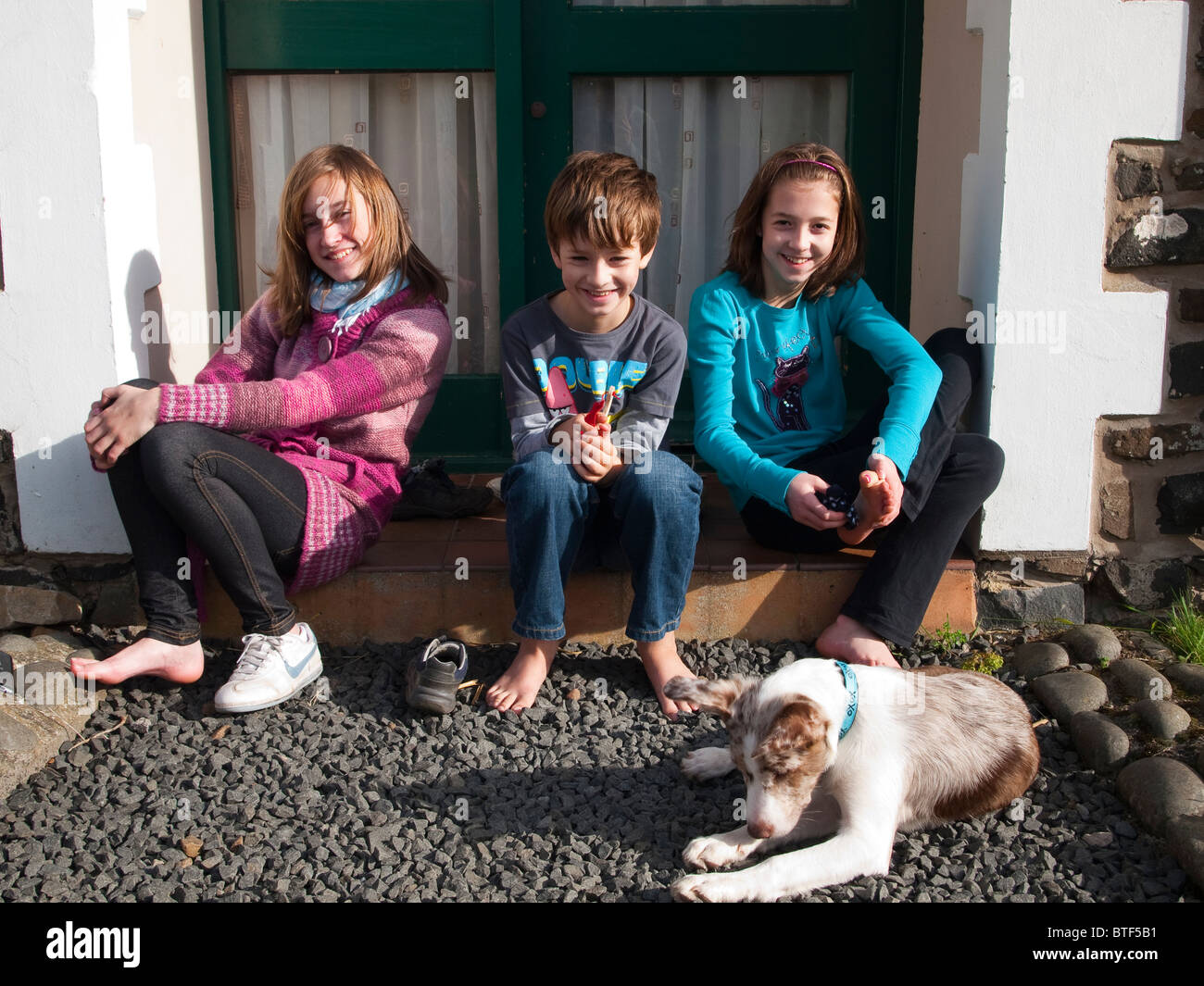 Drei Kinder und ihre Welpen sitzen vor einer Haustür Stockfoto
