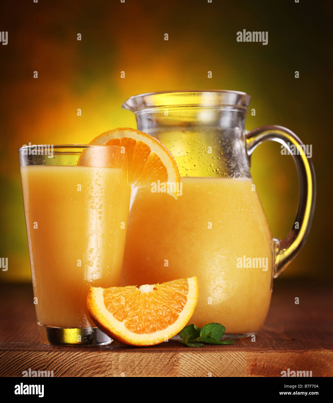 Stillleben: Orangen, Glas Saft und Krug voller Saft auf einem Holztisch. Stockfoto