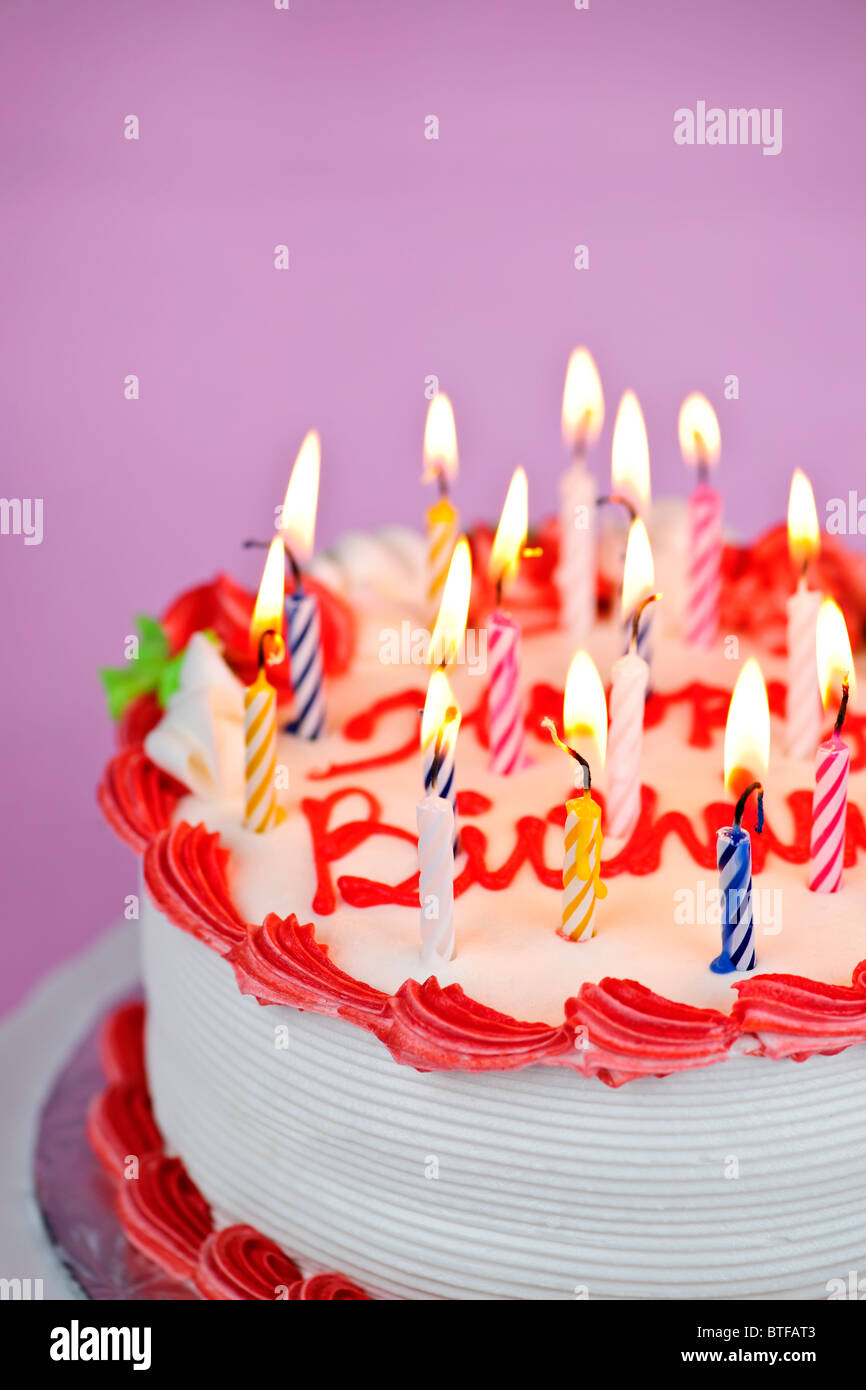 Geburtstagstorte mit brennenden Kerzen und Sahnehäubchen auf rosa Hintergrund Stockfoto