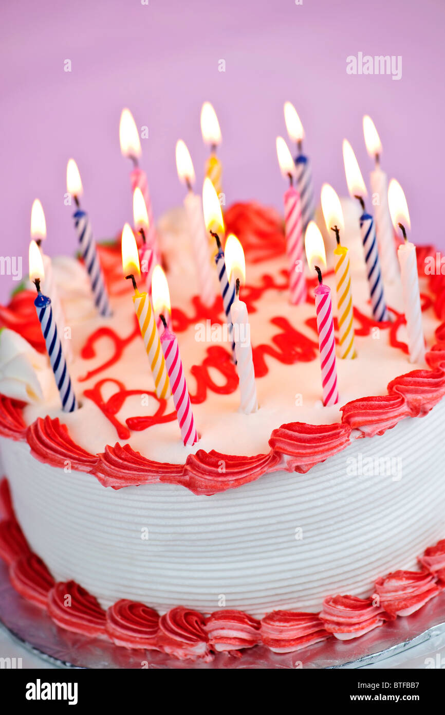 Geburtstagstorte mit brennenden Kerzen und Sahnehäubchen auf rosa Hintergrund Stockfoto