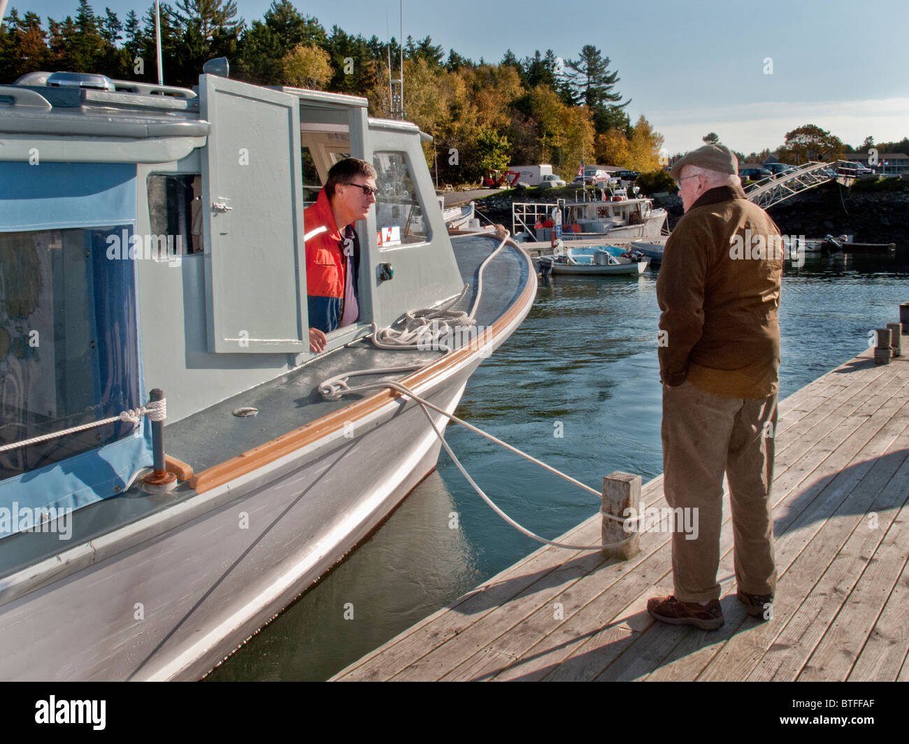 Der Kapitän von einem Ausflugsboot plaudert mit einem älteren Passanten auf dem Pier in North East Harbor, Maine. Stockfoto