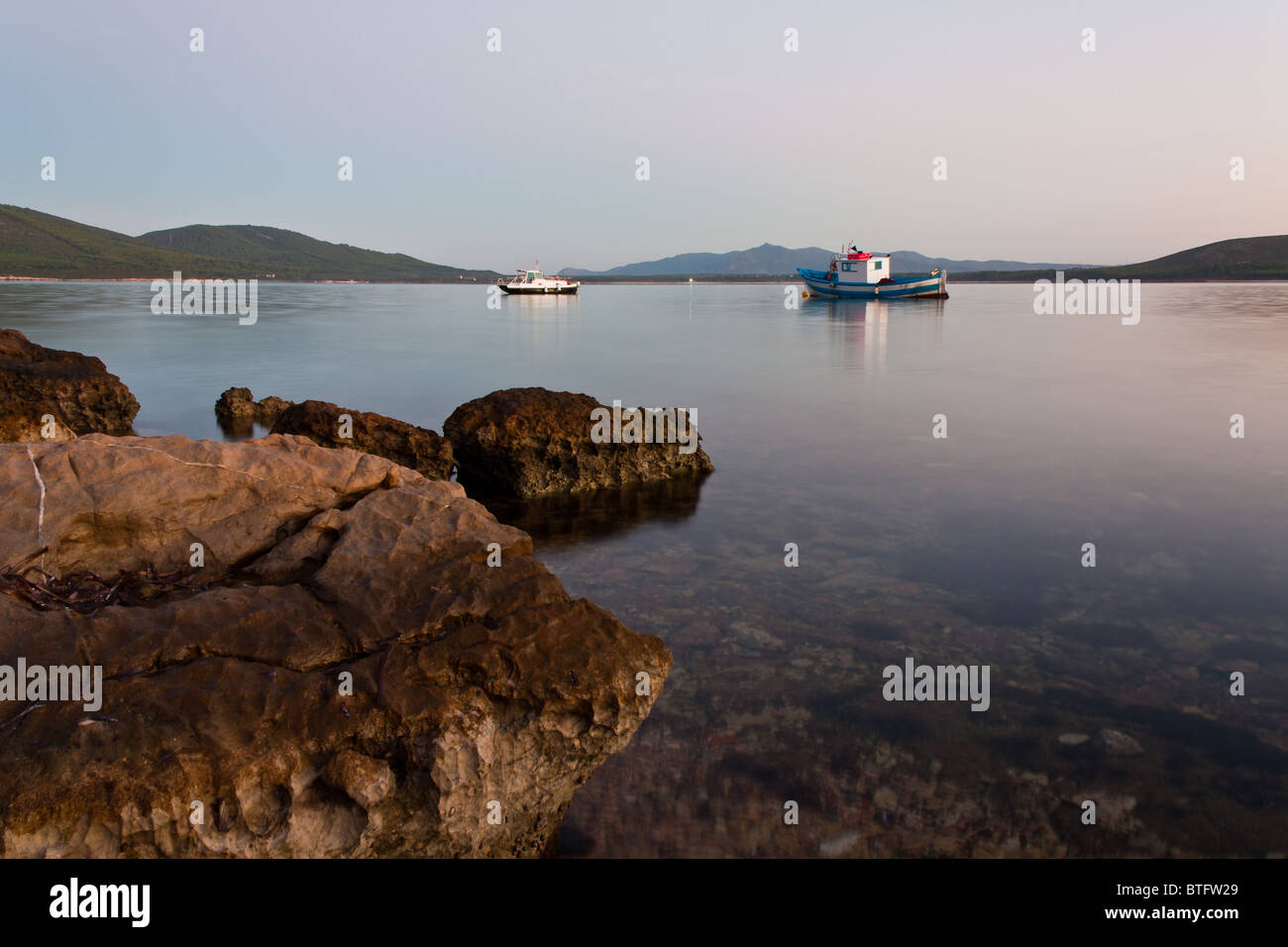 zwei Schiffe in einem Hafen in der Morgendämmerung mit Felsen im Vordergrund Stockfoto