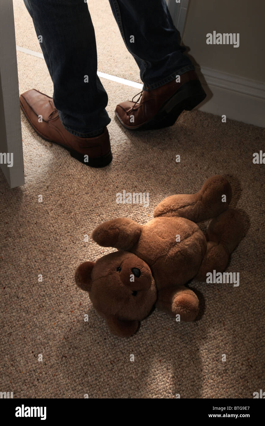 Des Kindes Teddybär liegend auf dem Boden ein Zimmer mit Teppichboden als eines Mannes Füße Schritt durch eine offene Tür Stockfoto