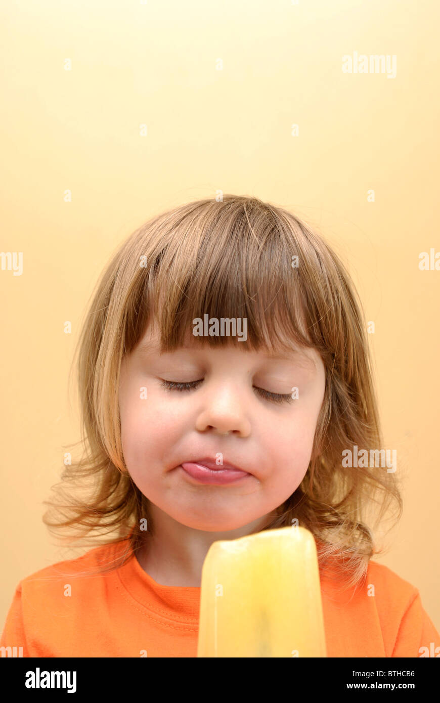 Drei Jahre altes Mädchen essen eine orange Eis am Stiel mit einem verträumten Ausdruck und Kopie Raum. Stockfoto Drei Jahre altes Mädchen essen eine orange Eis am Stiel mit einem verträumten Ausdruck und Kopie Raum. Stockfoto