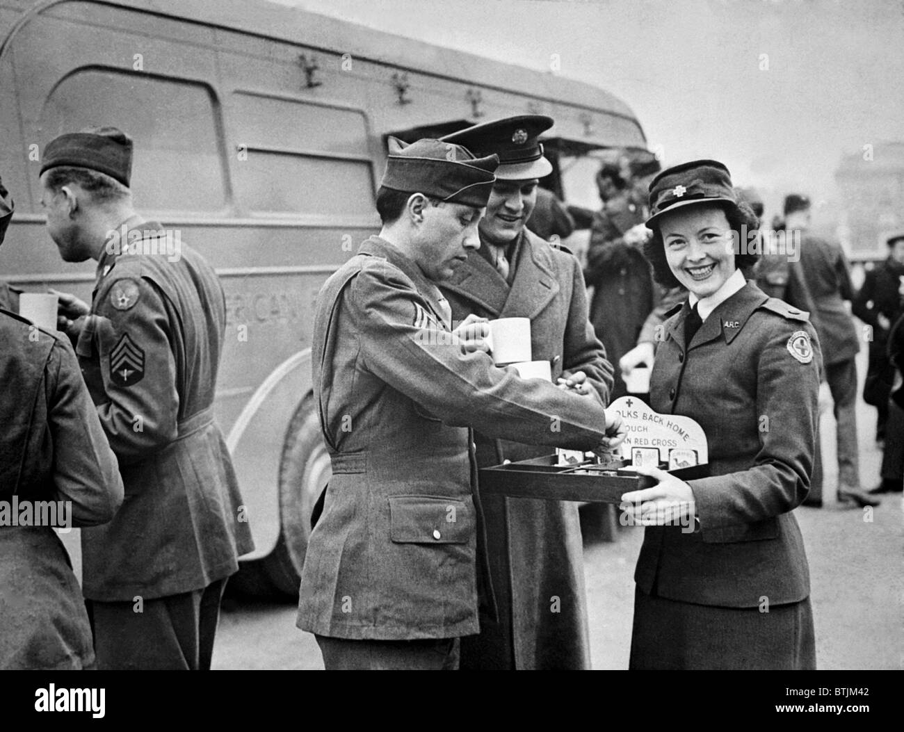 Ein rotes Kreuz Arbeiter lächelt als She-Angebote, die amerikanische Soldaten Süßigkeiten und Zigaretten nach der "Wings for Victory" Woche Feier in London, England, März 1943 Stockfoto