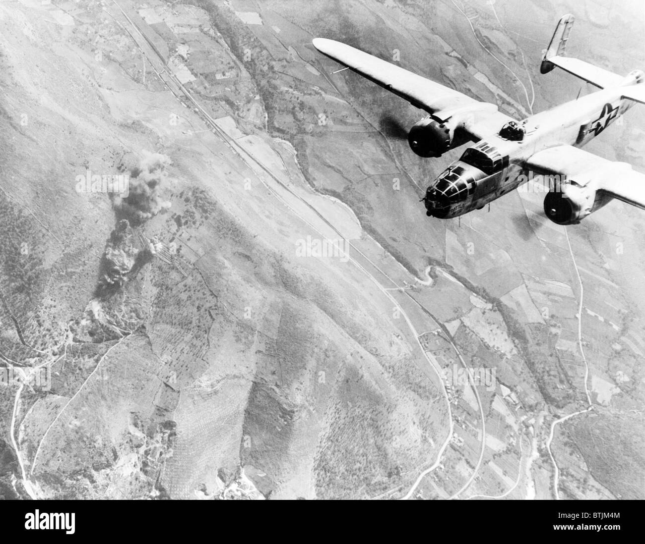 Ein Nazi-Versorgung-Dump geht in Rauch auf. Ein US-b-25 mittlerer Bomber brüllt über Tivoli, Nazi-Versorgungsmaterial-Mitte 10 Meilen östlich von Rom. Jetzt eine Rauchen-Ruine, es wurde von den deutschen als Terminal für routing Verstärkungen zu Schlacht Bereichen verwendet. Stockfoto