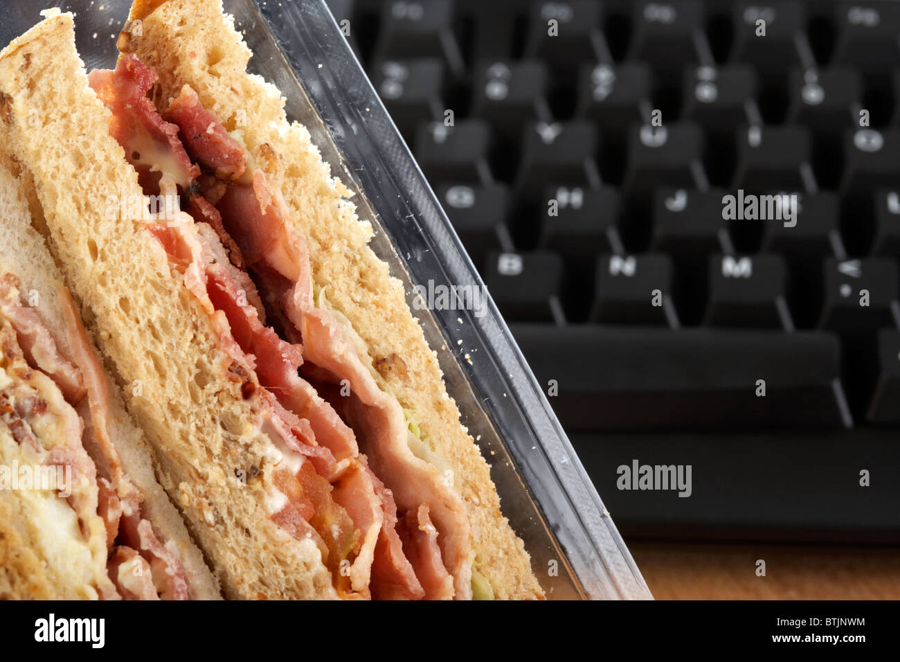 Take-away dreifach Sandwiches im Karton neben Computer-Tastatur zur Mittagszeit Stockfoto