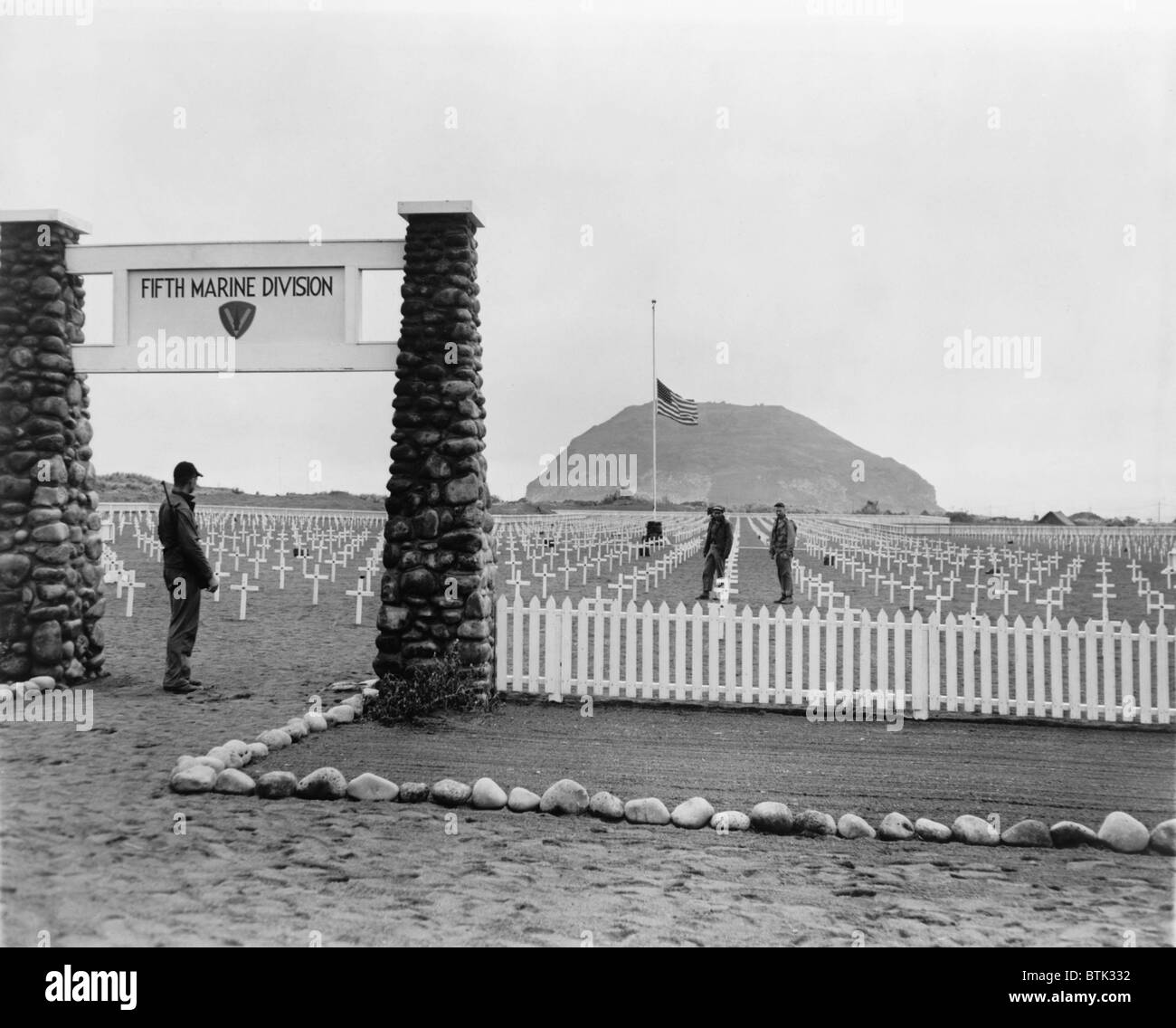 Iwo Jima im April 1945. Marine Friedhof, wo US-Marines getötet in der Schlacht von Iwo Jima begraben wurden. Amerikanische Flagge auf Halbmast in Gedenken an den verstorbenen Präsidenten Roosevelt und Mount Suribachi sind im Hintergrund. Stockfoto