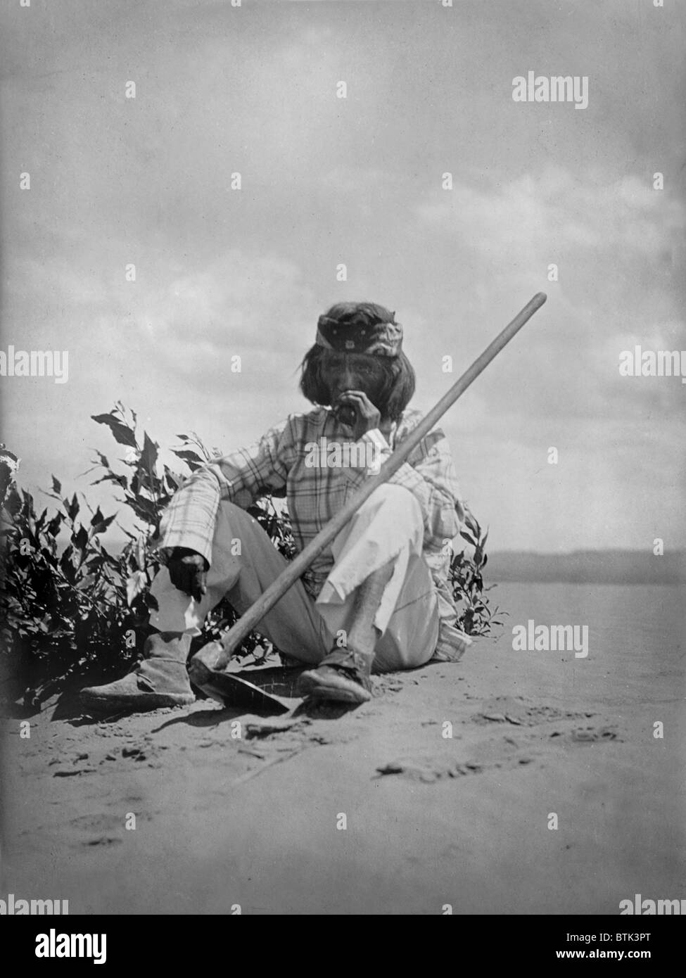Hopi Mann sitzt auf dem Boden Rauchen mit Hacke gelehnt auf seinem linken Knie, Originaltitel: "Ein ruhiger Rauch Hopi", Foto von Curtis, 1907 Stockfoto