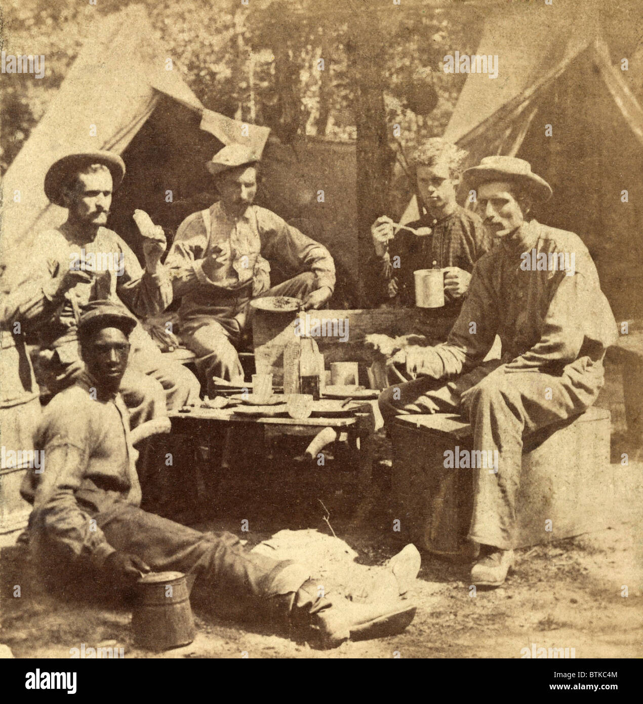 Entspannte Szene von Soldaten der Armee des Potomac essen ihre Mahlzeit in der Gesellschaft von Afro-Amerikaner, wahrscheinlich ein "Schmuggelware," eingesetzt, um zu kochen und die Arbeiten für die Soldaten. Ca. 1862-65. Stockfoto