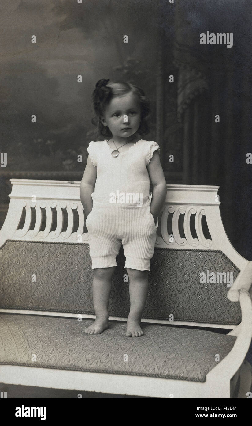 Historisches Foto (1910) von einem Mädchen steht auf einer Bank Stockfoto