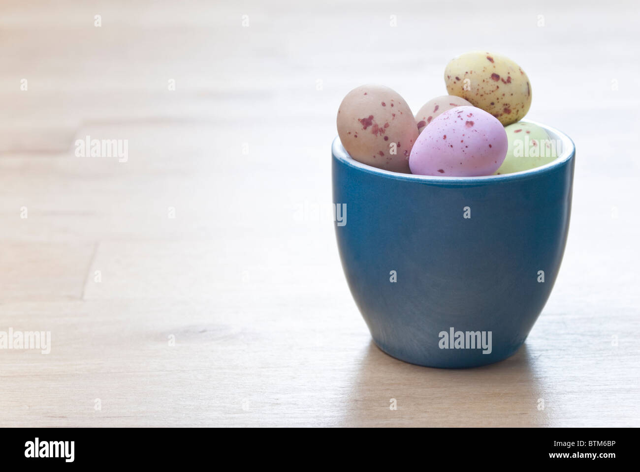 Ein Eierbecher, gefüllt mit bunten Osterei Süßigkeiten, auf einem Holztisch Birke. Kopieren Sie Raum auf der linken Seite. Stockfoto